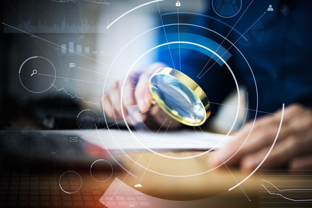 A person is holding a magnifying glass in front of a laptop computer.