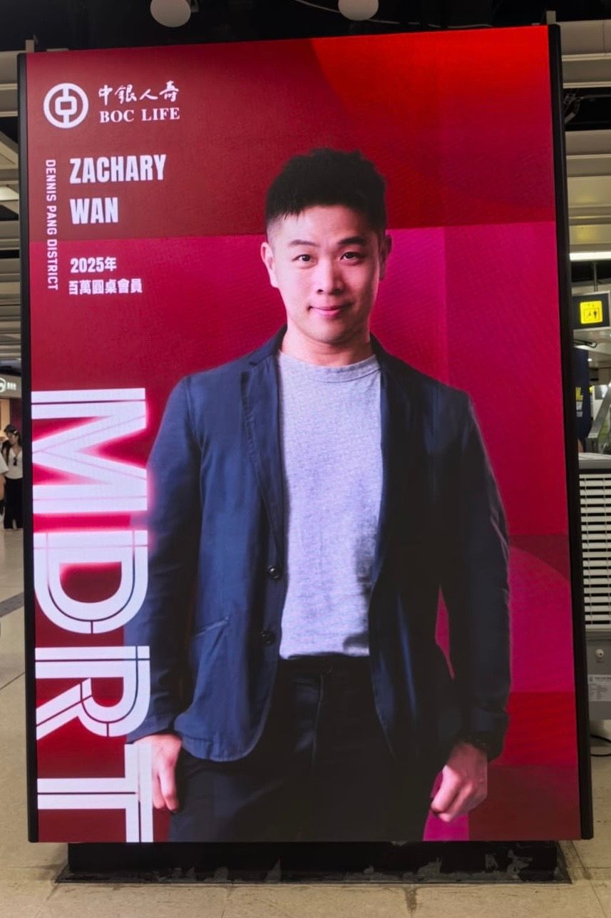 A man in a blue blazer and bow tie poses with a thumbs-up next to banners for COT, TOT, and MDRT.