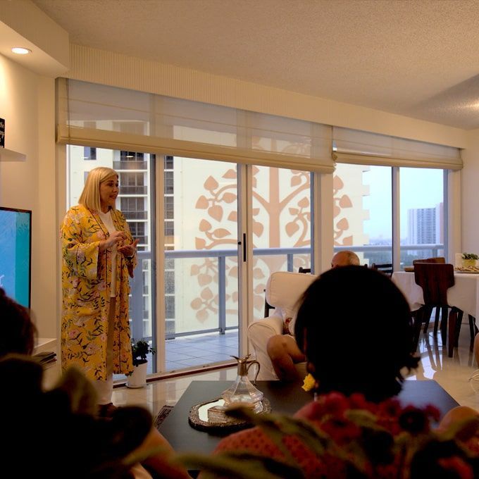 Una mujer está parada en una sala de estar hablando con un grupo de personas.