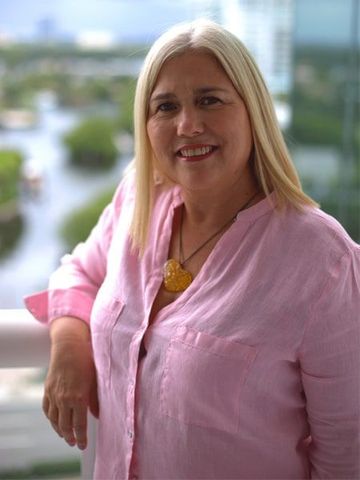 Una mujer con una camisa rosa está apoyada en una barandilla y sonríe.