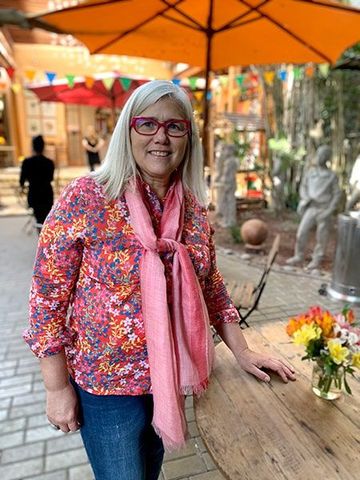 Una mujer que lleva gafas y una bufanda rosa está parada frente a una mesa.