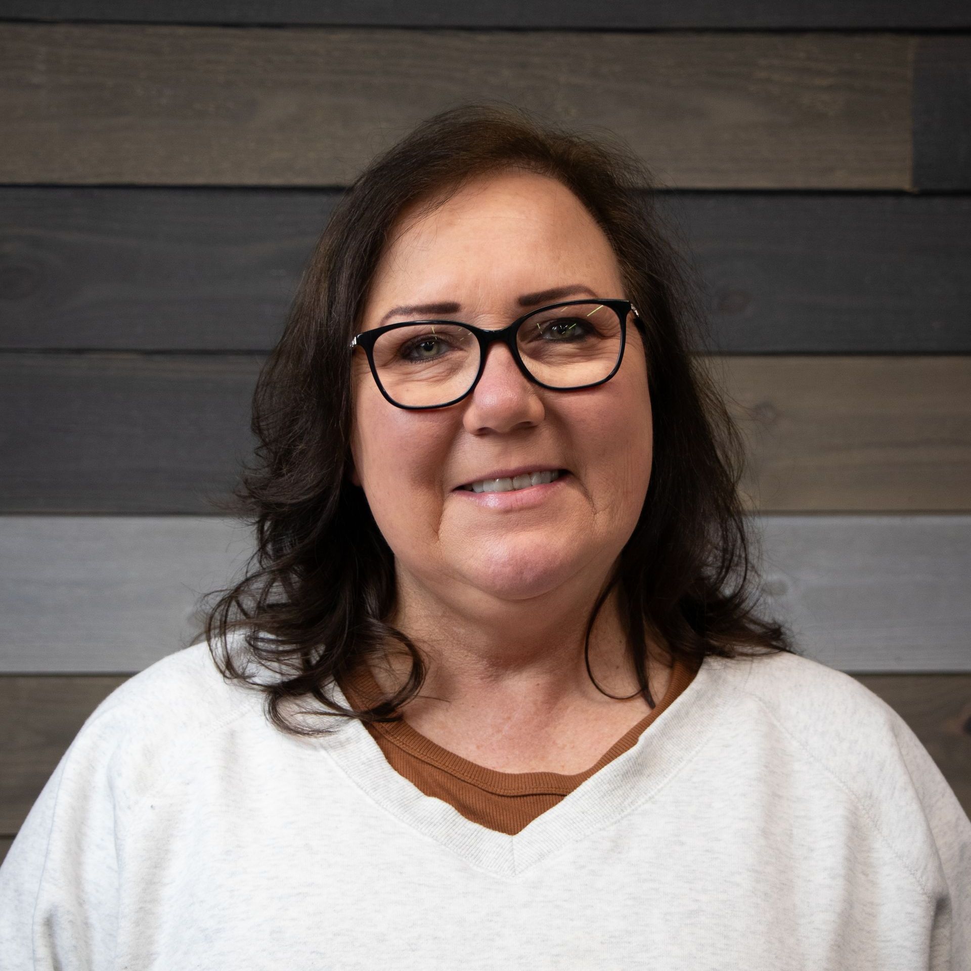 A woman wearing glasses and a white sweater is smiling for the camera.