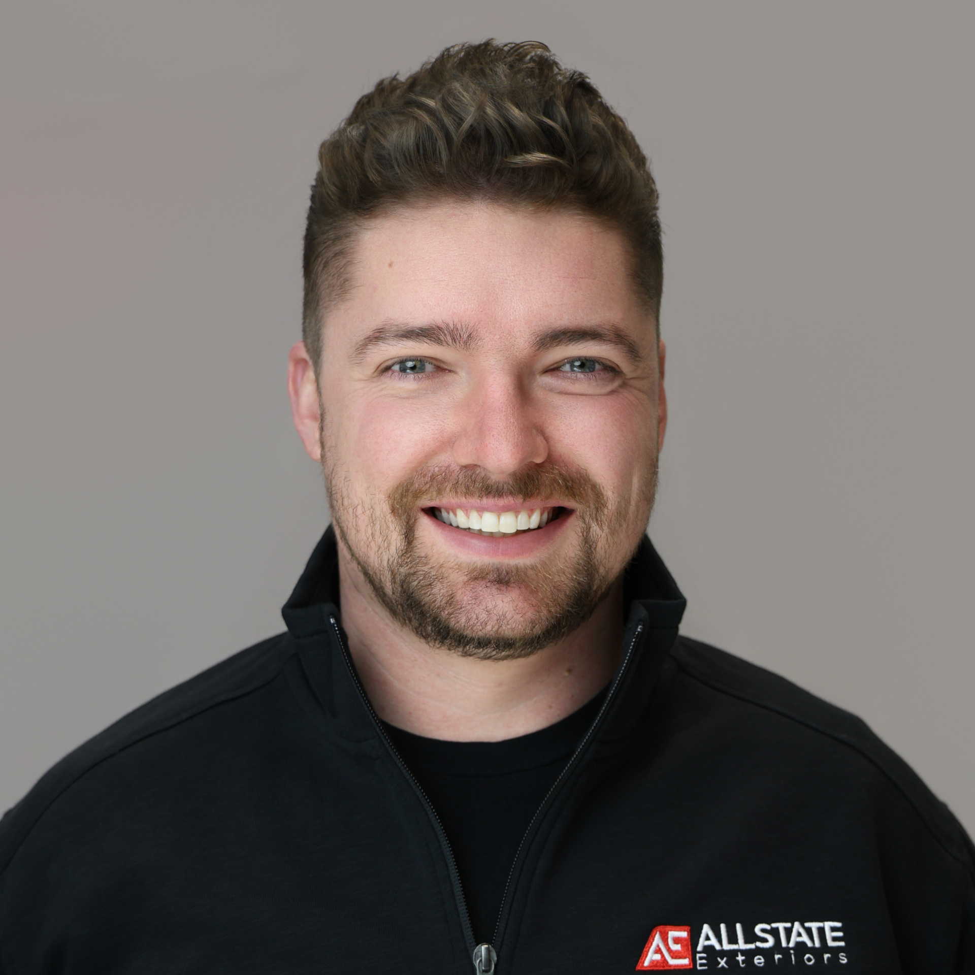 A man with green eyes and a beard smiling to the camera.