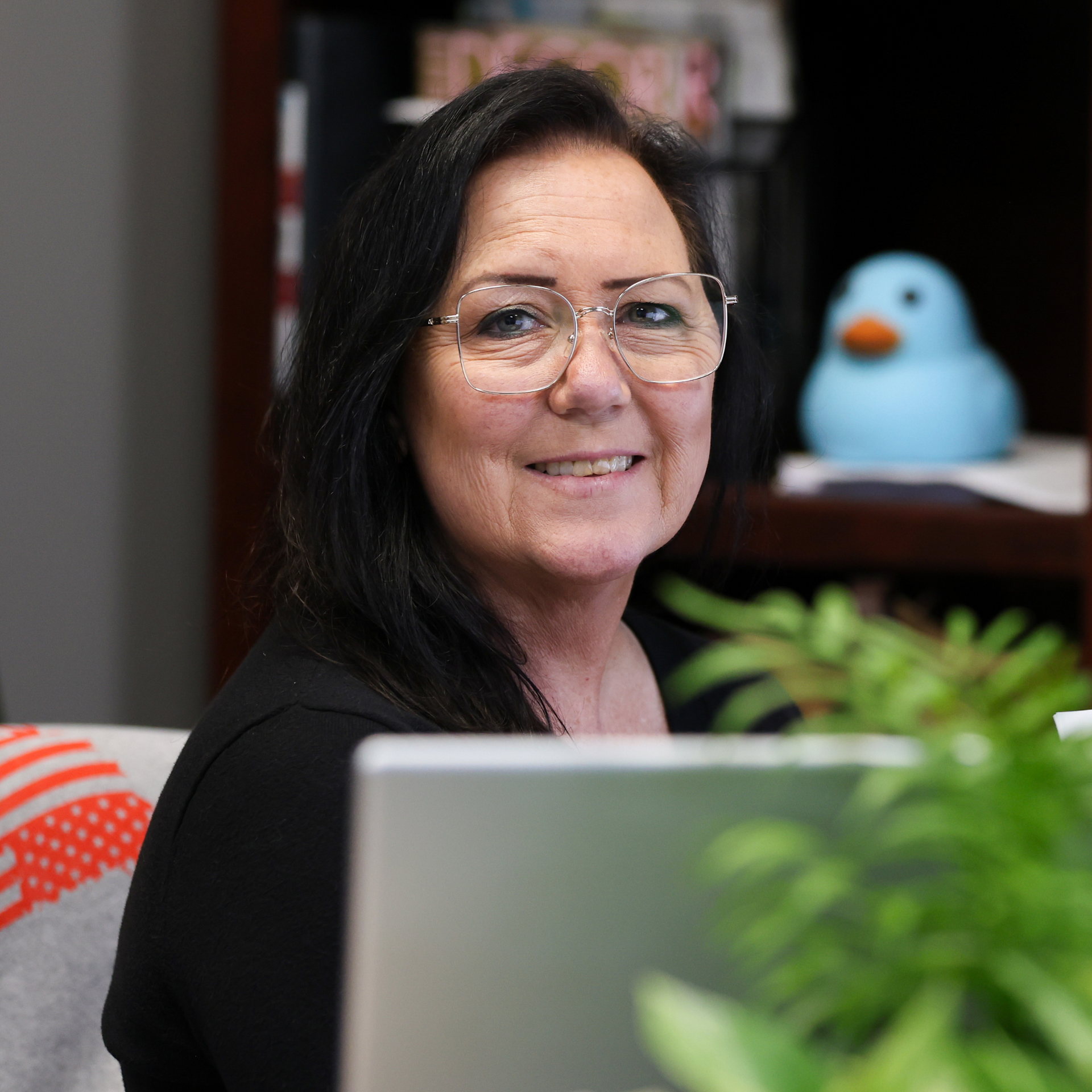 A woman wearing glasses and a white sweater is smiling for the camera.