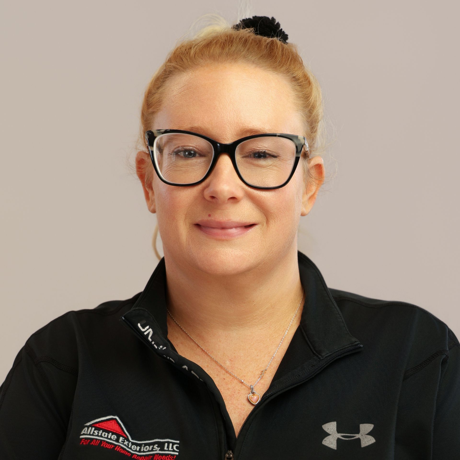 A woman wearing glasses and a black polo shirt is smiling for the camera.