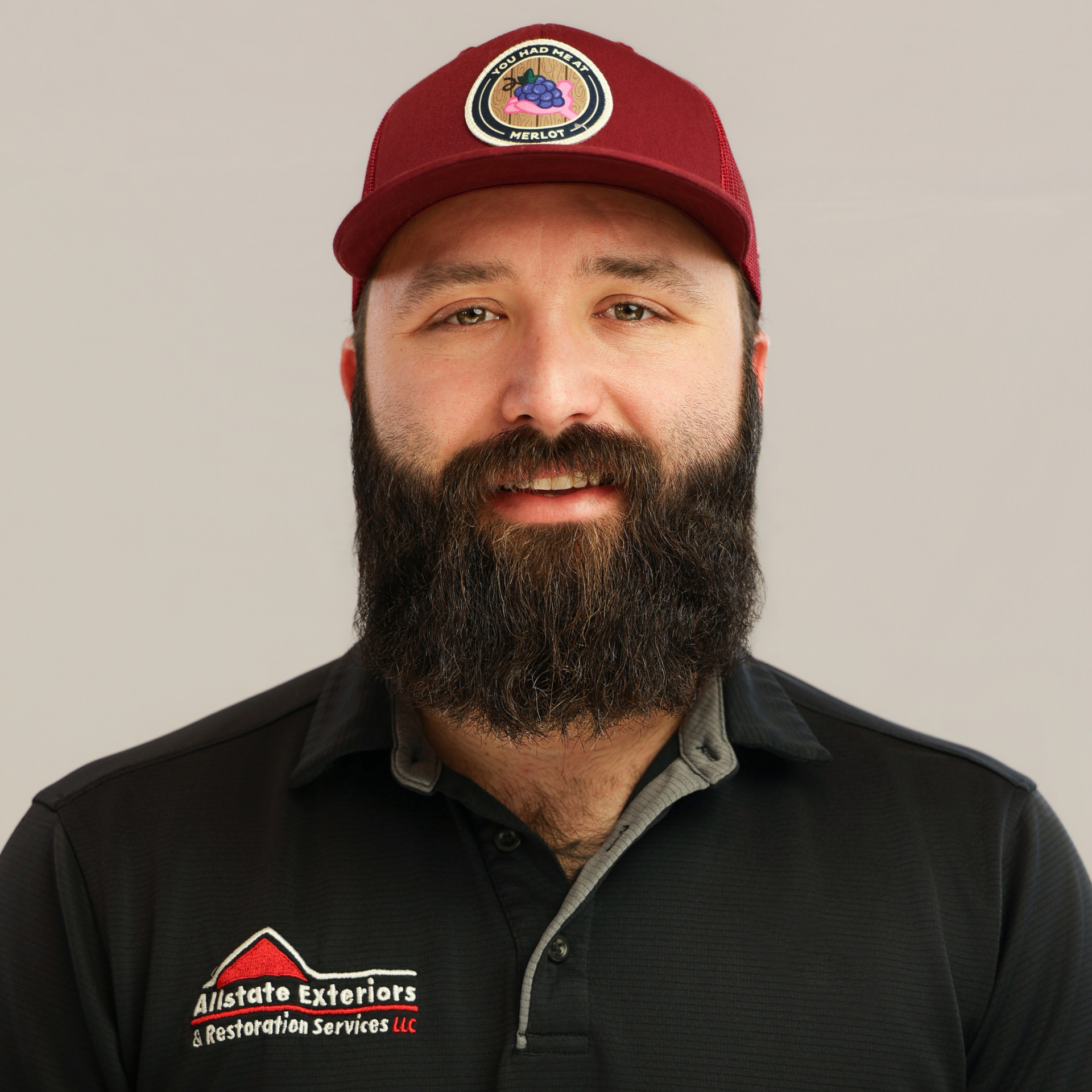 A man with a beard and a hat is standing in a field with his arms crossed.