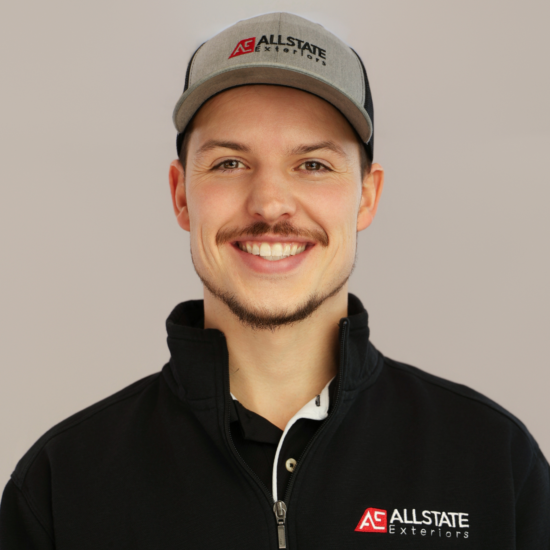 A man in a black shirt is standing in a field with his arms crossed and smiling.