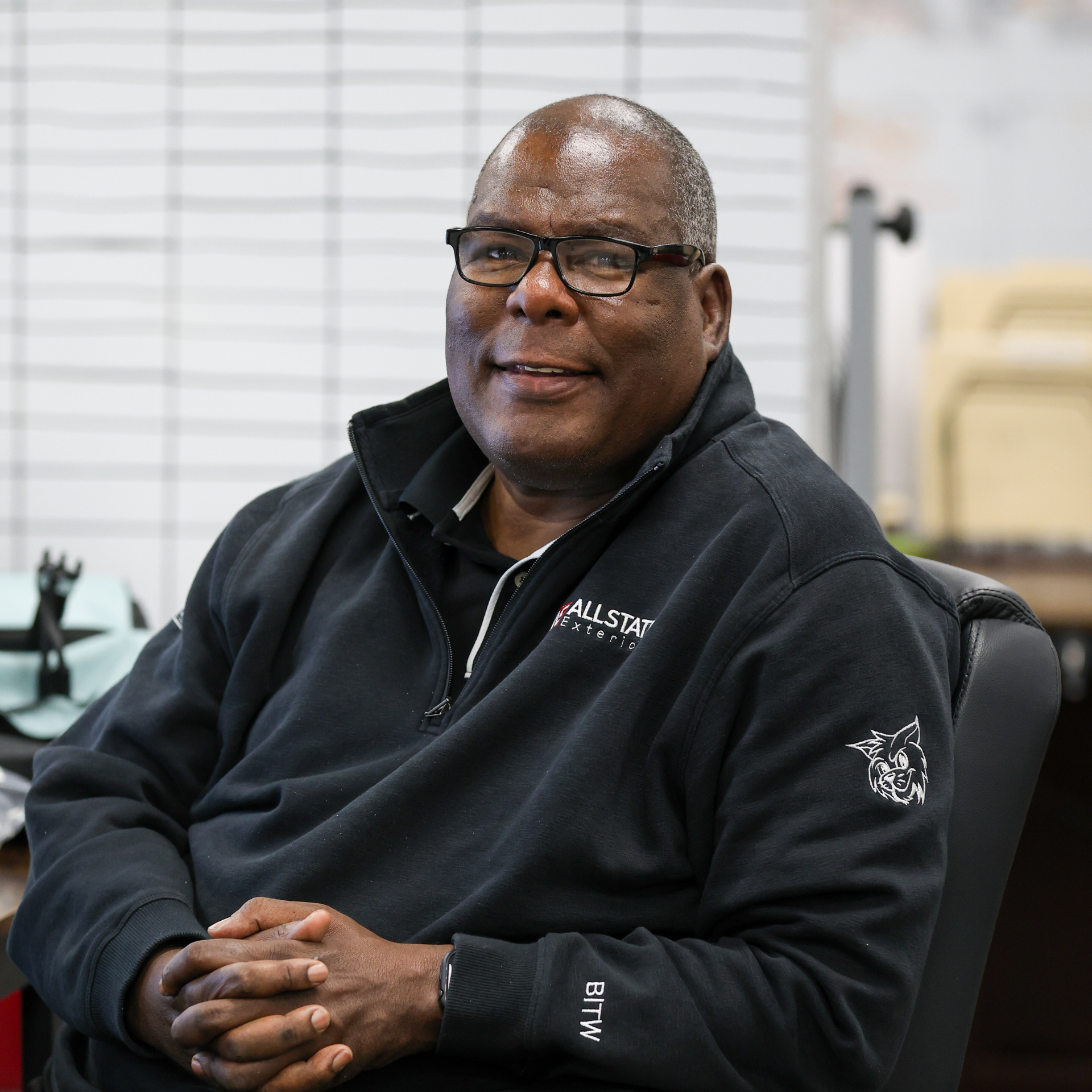 A man wearing a red shirt and a black vest is standing in front of a field of tall grass.