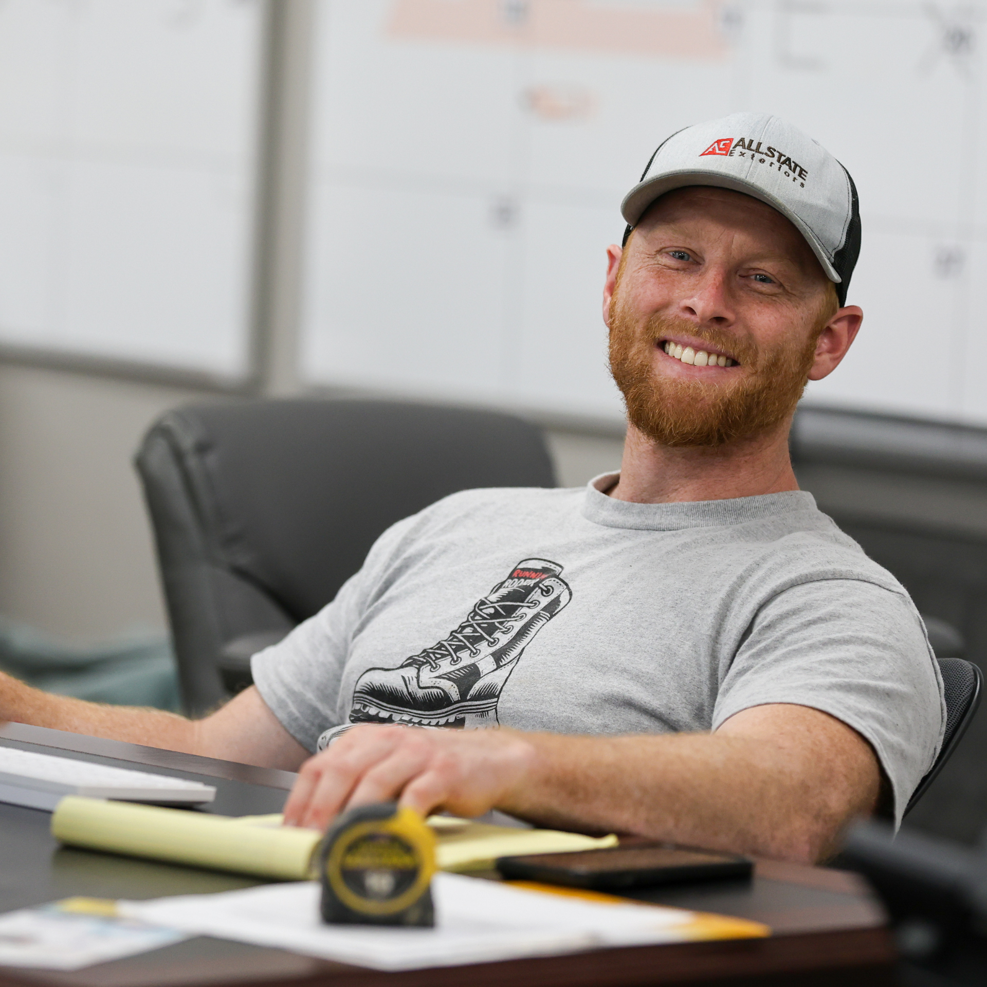 A man with a beard is wearing a grey t-shirt and smiling.