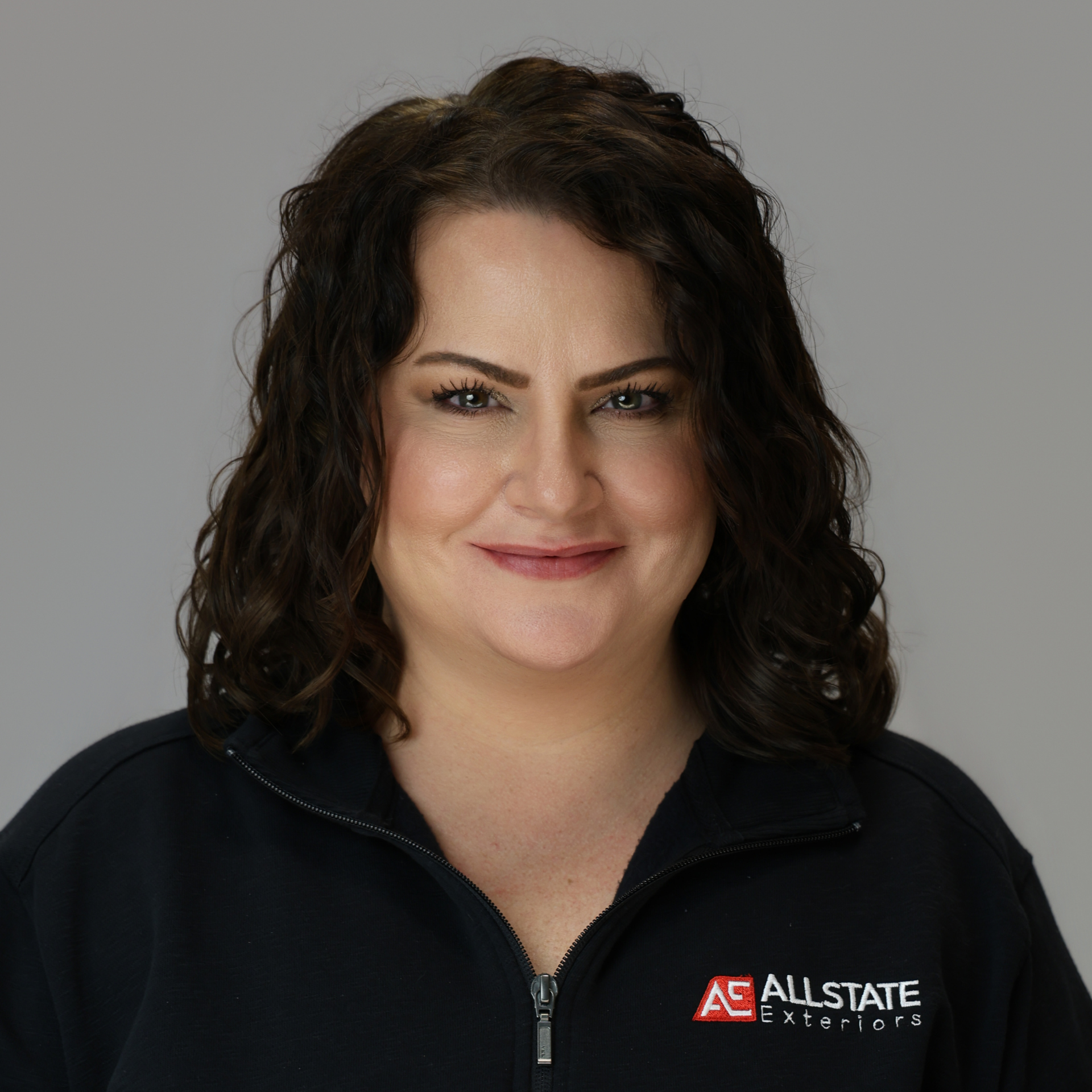 A woman with long hair is smiling in a field of tall grass.