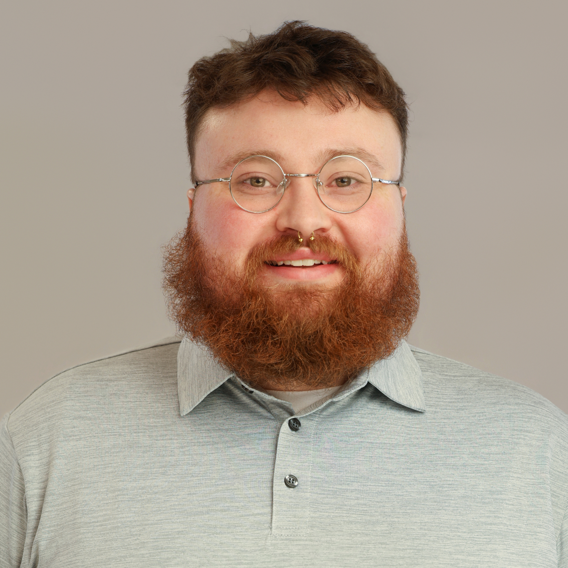 A man with red hair, and a beard smiling to the camera.