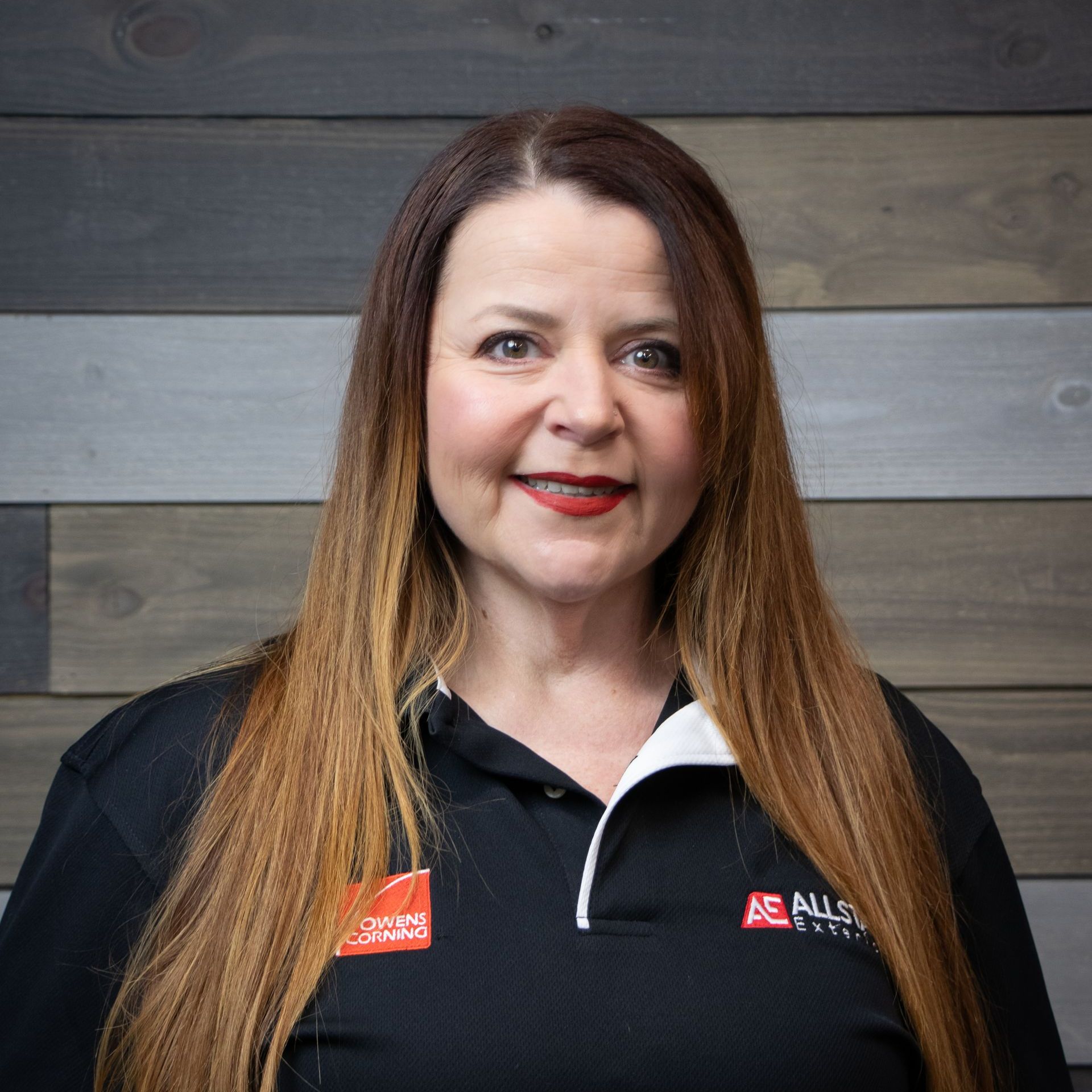 A woman with long hair is wearing a black shirt and smiling.