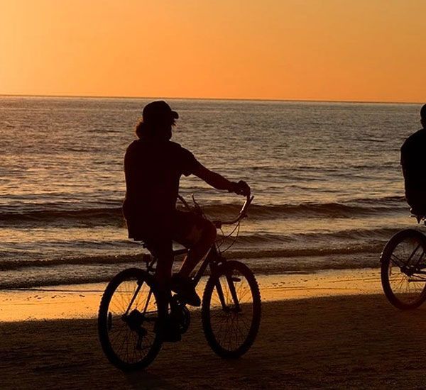 Two people riding bicycles on the beach at sunset
