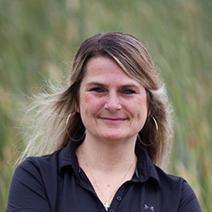 a woman in a black shirt is standing in a field with her arms crossed and smiling