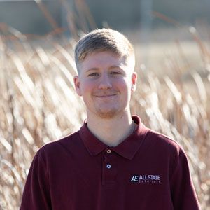 A young man in a maroon polo shirt is standing in a field of tall grass.