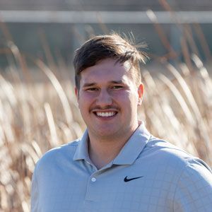 A man in a nike shirt is smiling in a field of tall grass.