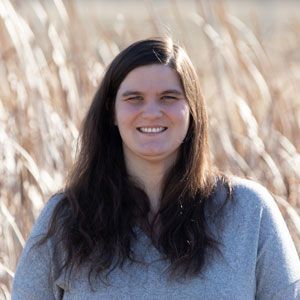 A woman with long hair is smiling in a field of tall grass.