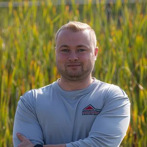 A man with his arms crossed is standing in front of a field of tall grass.