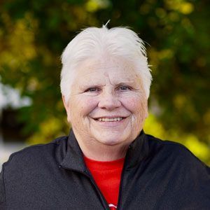 A woman with white hair is smiling for the camera while wearing a black jacket and a red shirt.