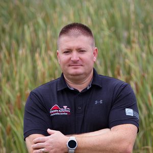 A man in a black shirt is standing in a field with his arms crossed.