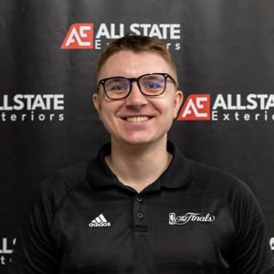 A man wearing glasses is smiling in front of an allstate banner