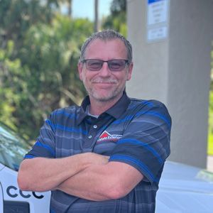 A man wearing glasses is standing in front of a white van with his arms crossed.