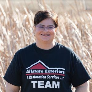 a woman wearing a black allstate exteriors & restoration services t-shirt is standing in a field