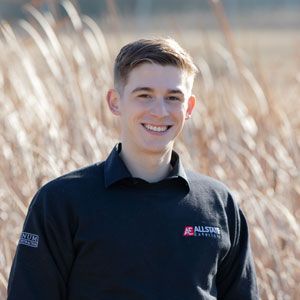 A young man is standing in a field of tall grass and smiling.