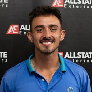 A man in a blue shirt is smiling in front of an allstate sign