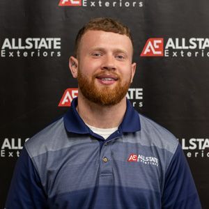 A man with a beard is wearing a blue and gray polo shirt.