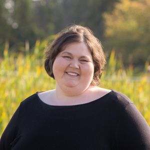 A woman in a black shirt is smiling in a field of tall grass.