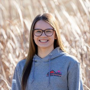 a woman wearing glasses and a hoodie is smiling in a field of tall grass