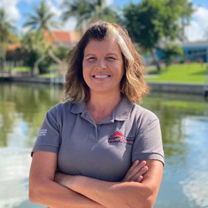 A woman is standing in front of a body of water with her arms crossed and smiling.