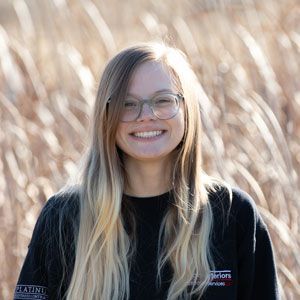 a young woman wearing glasses and a black shirt is smiling in front of tall grass