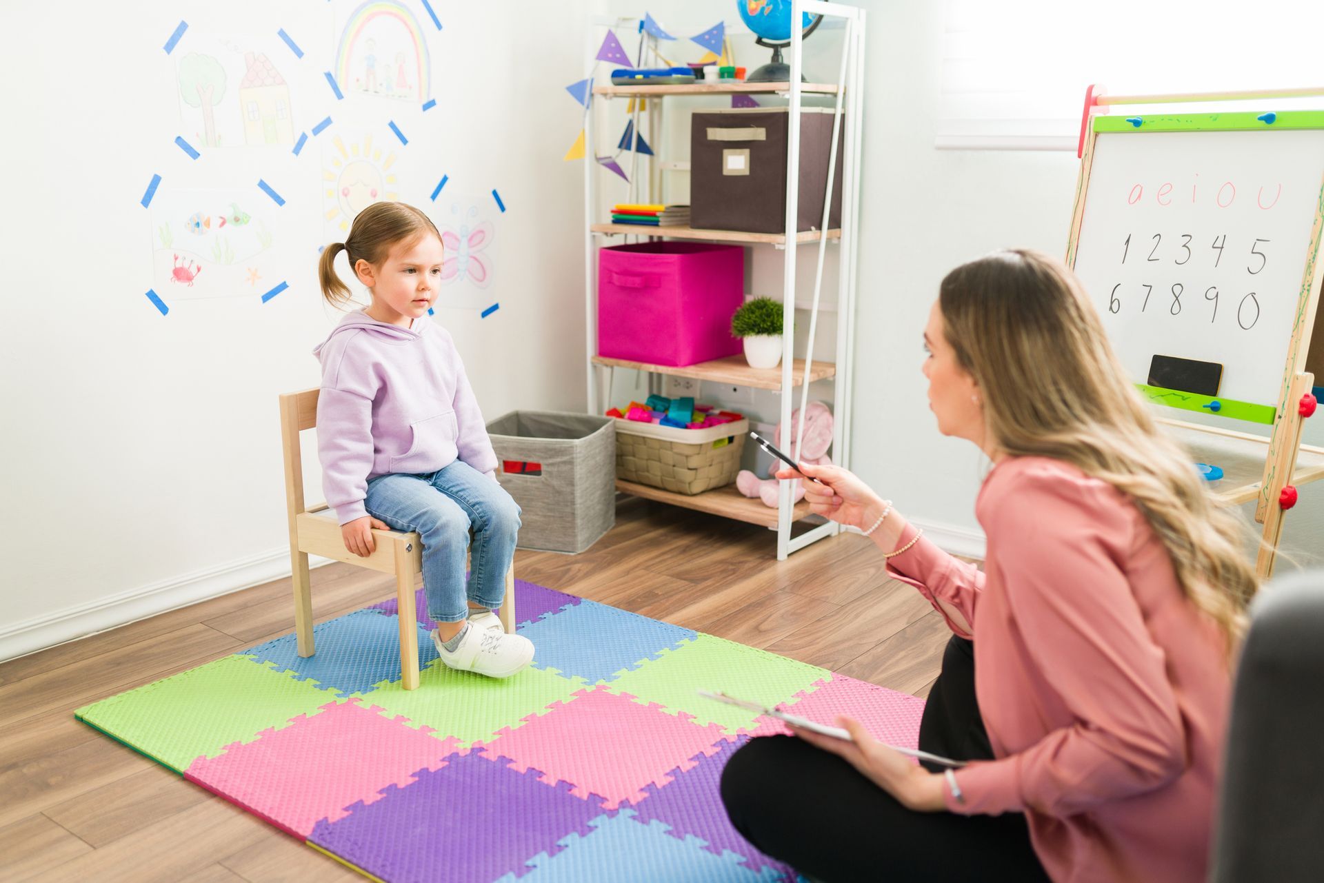 A woman is sitting on the floor talking to a little girl who is sitting in a chair.