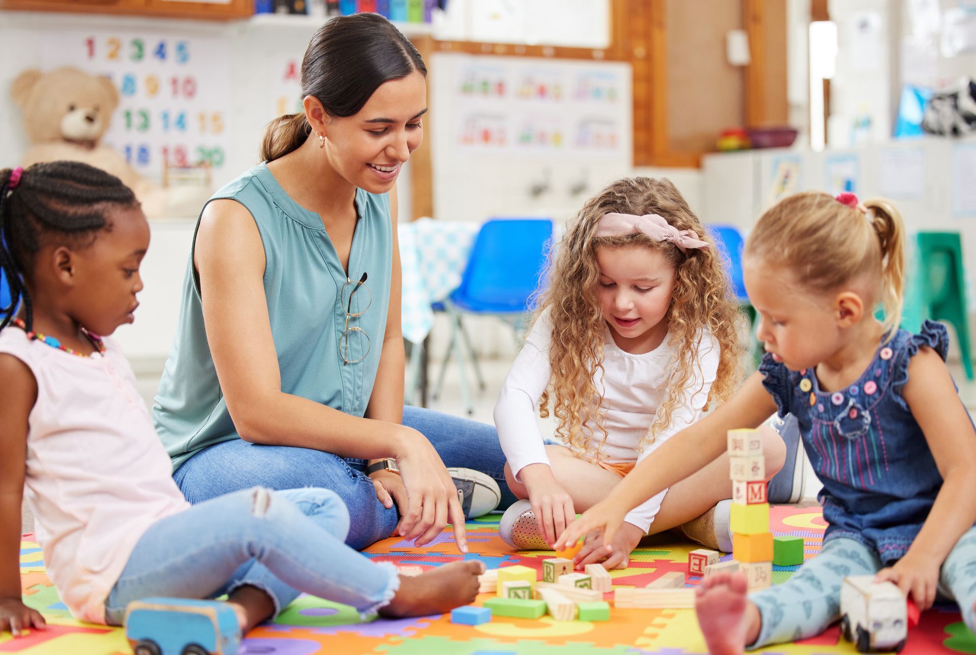 A group of young girls are sitting on the floor playing with blocks.