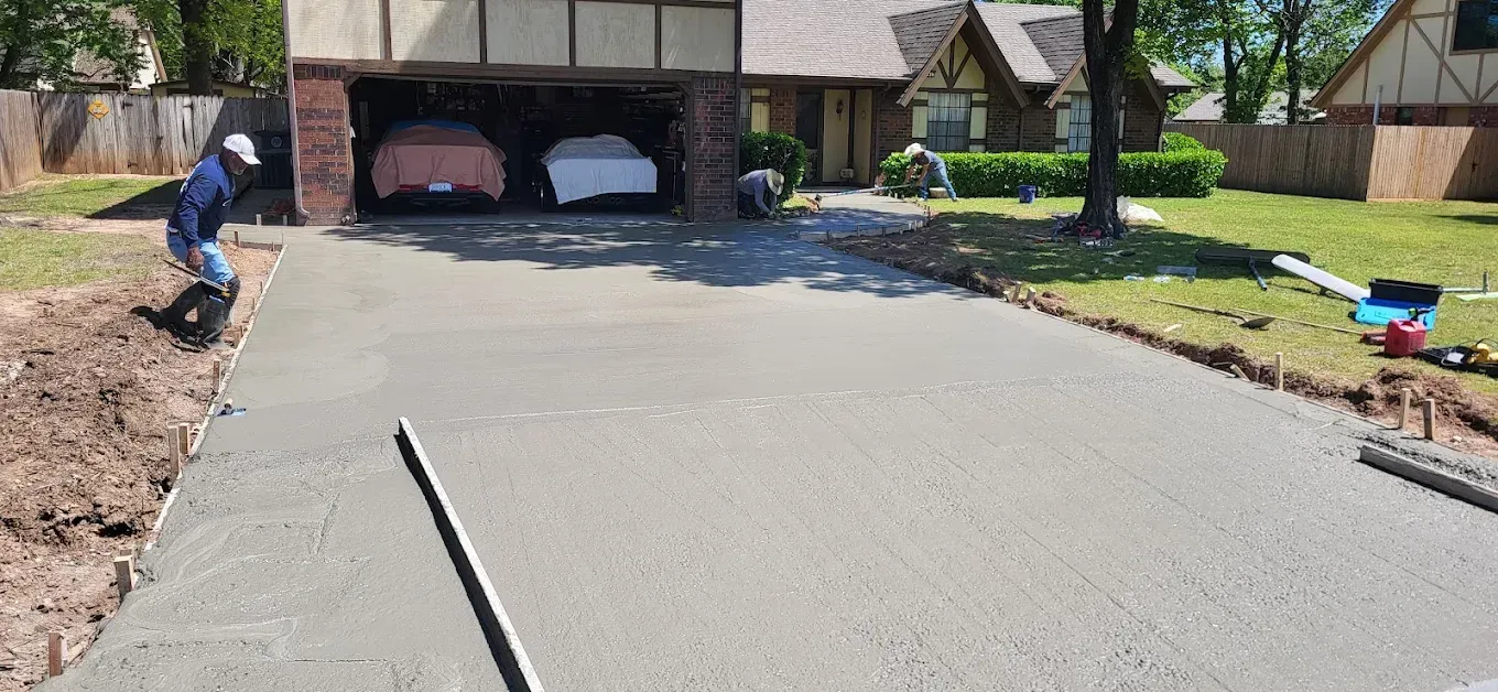 Workers pouring and spreading wet concrete on a sidewalk; construction site.