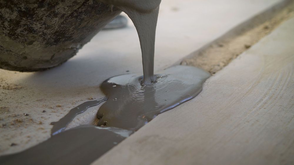 Pouring gray sealant into a long crack on a light-colored surface.