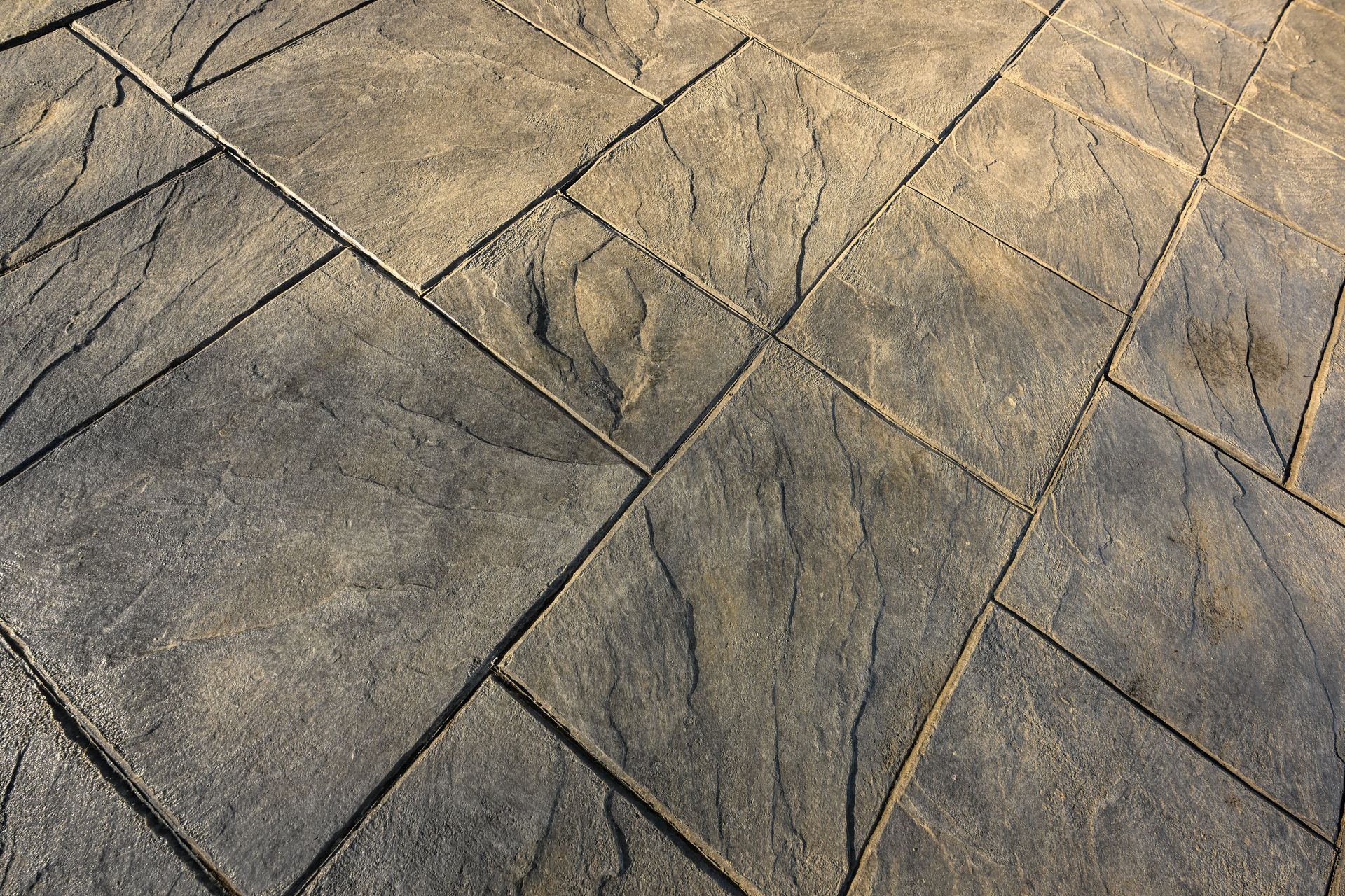 Close-up of gray stone paving tiles arranged in a diagonal pattern, textured with veins.