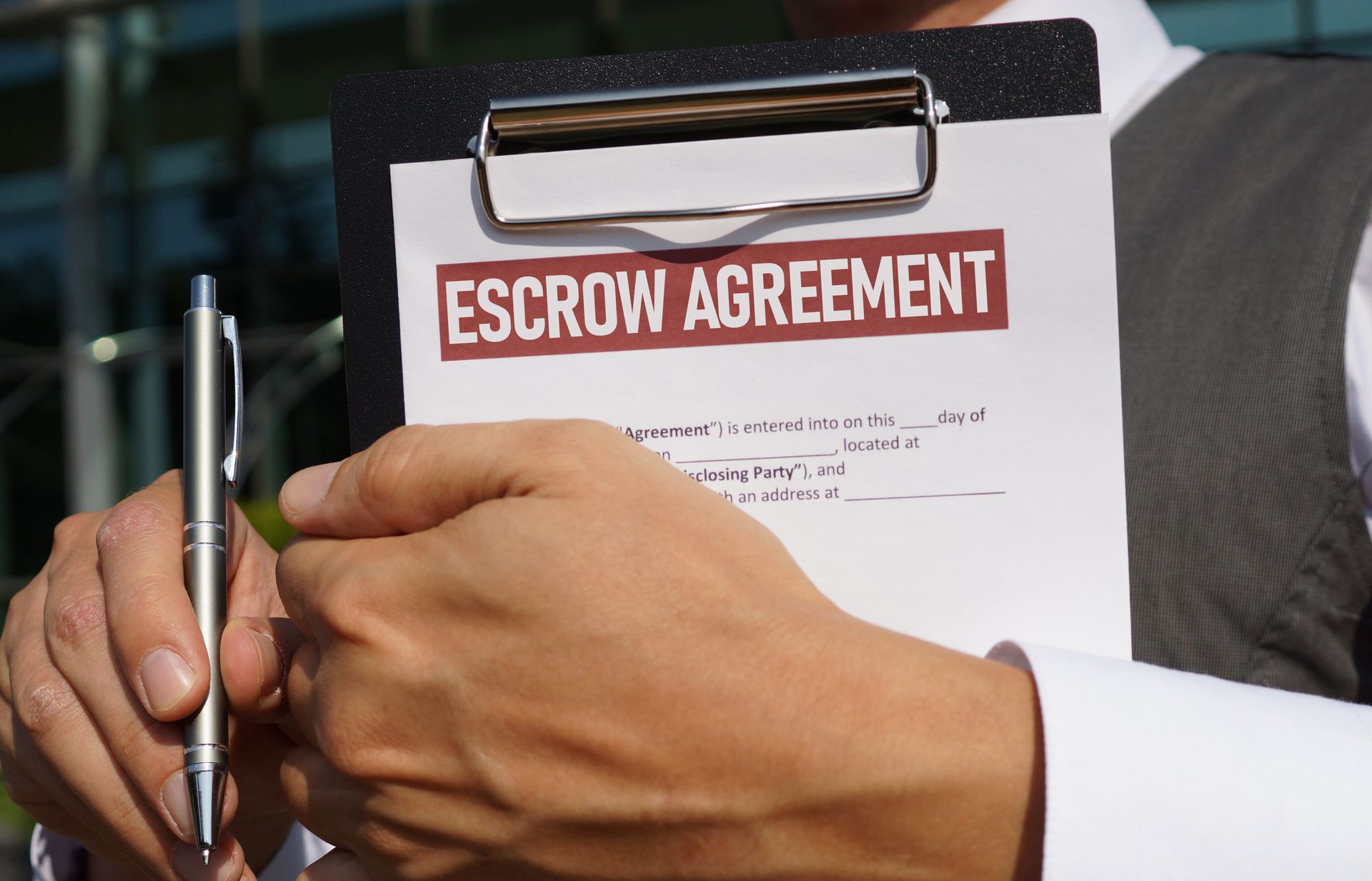 Person holding an escrow agreement on a clipboard with a pen. Person holding an escrow agreement on a clipboard with a pen.