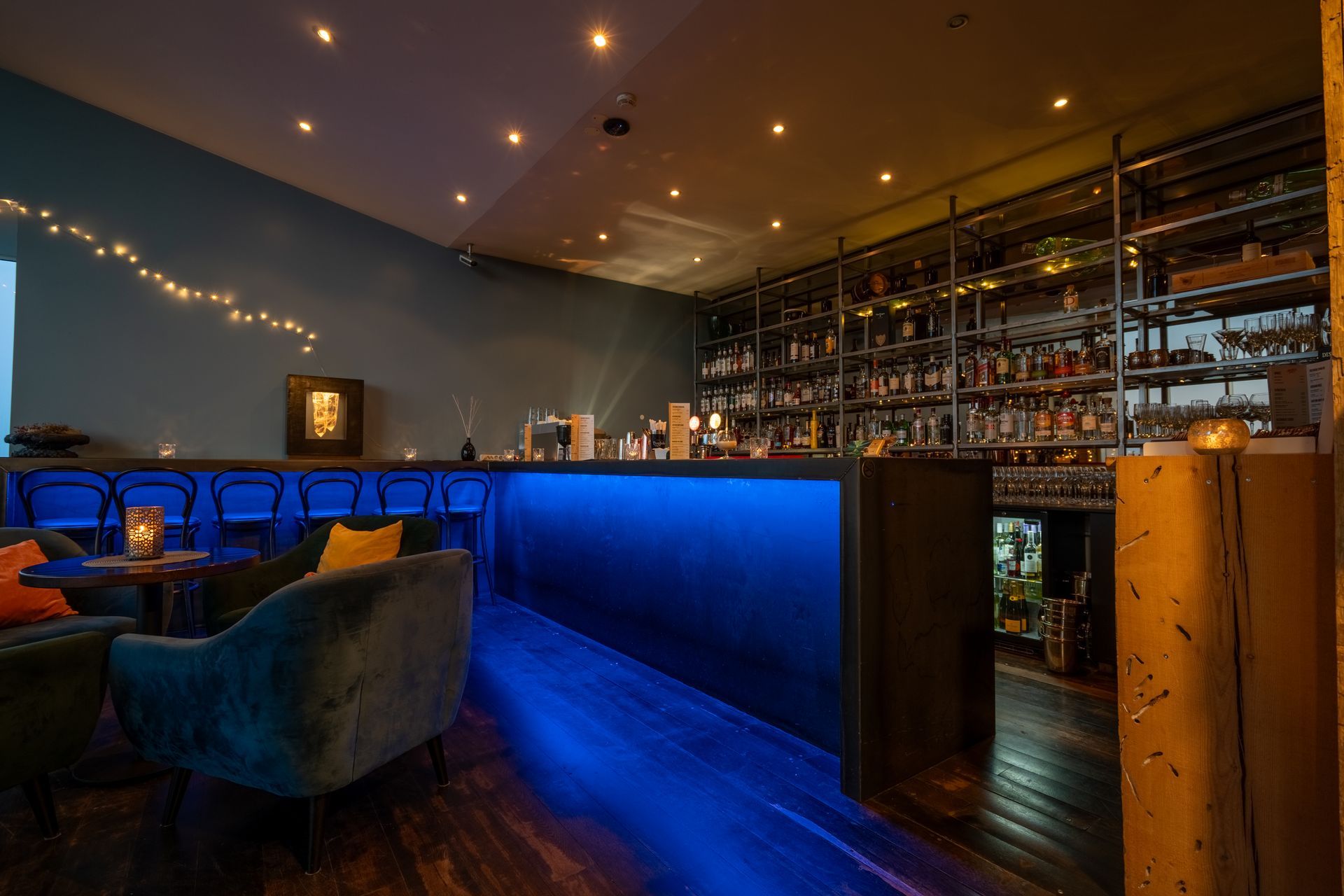 A bar with blue lights on the floor and a couch.