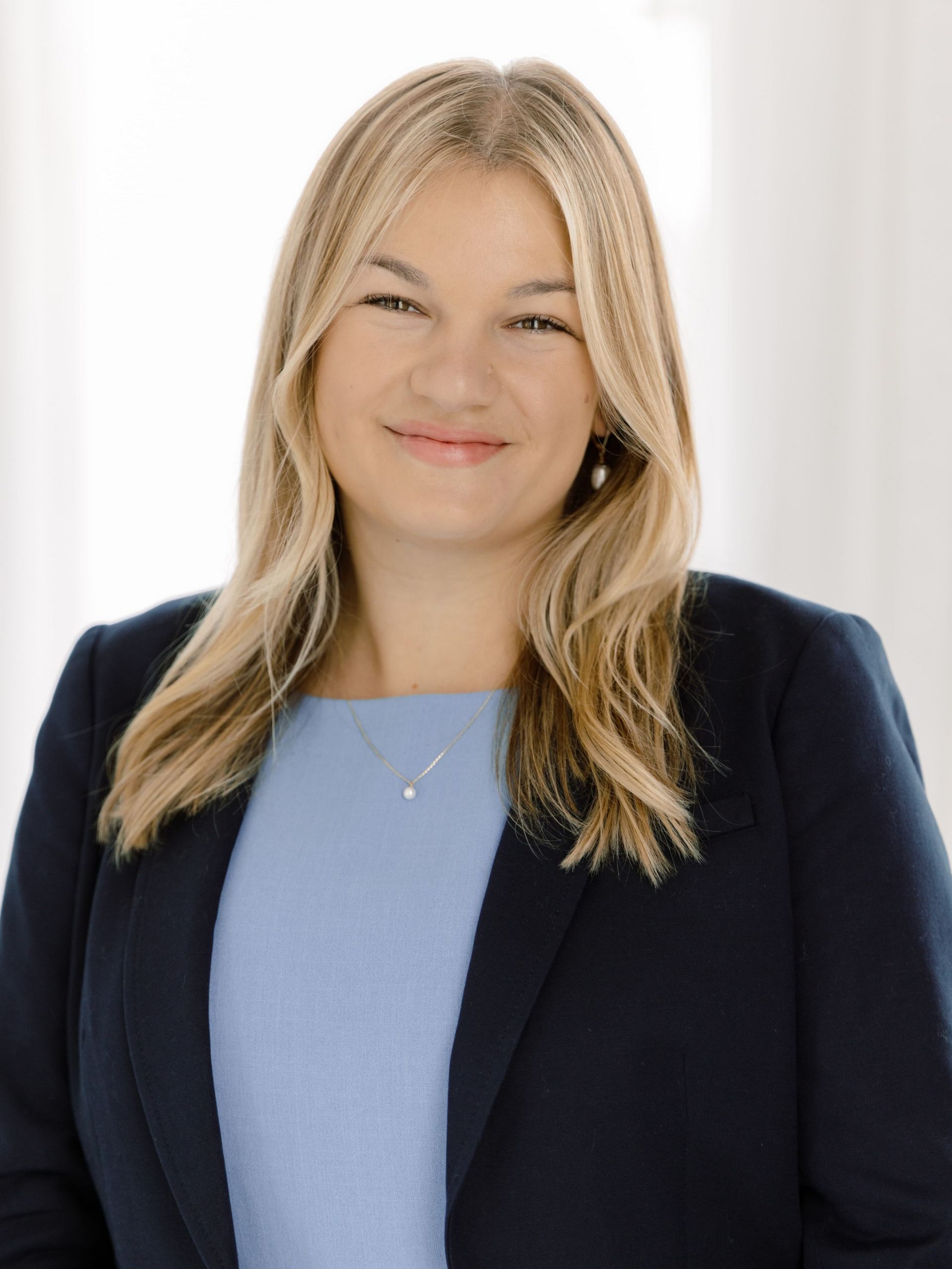 Woman with blonde hair wearing a blue blazer and top smiles against a light background.