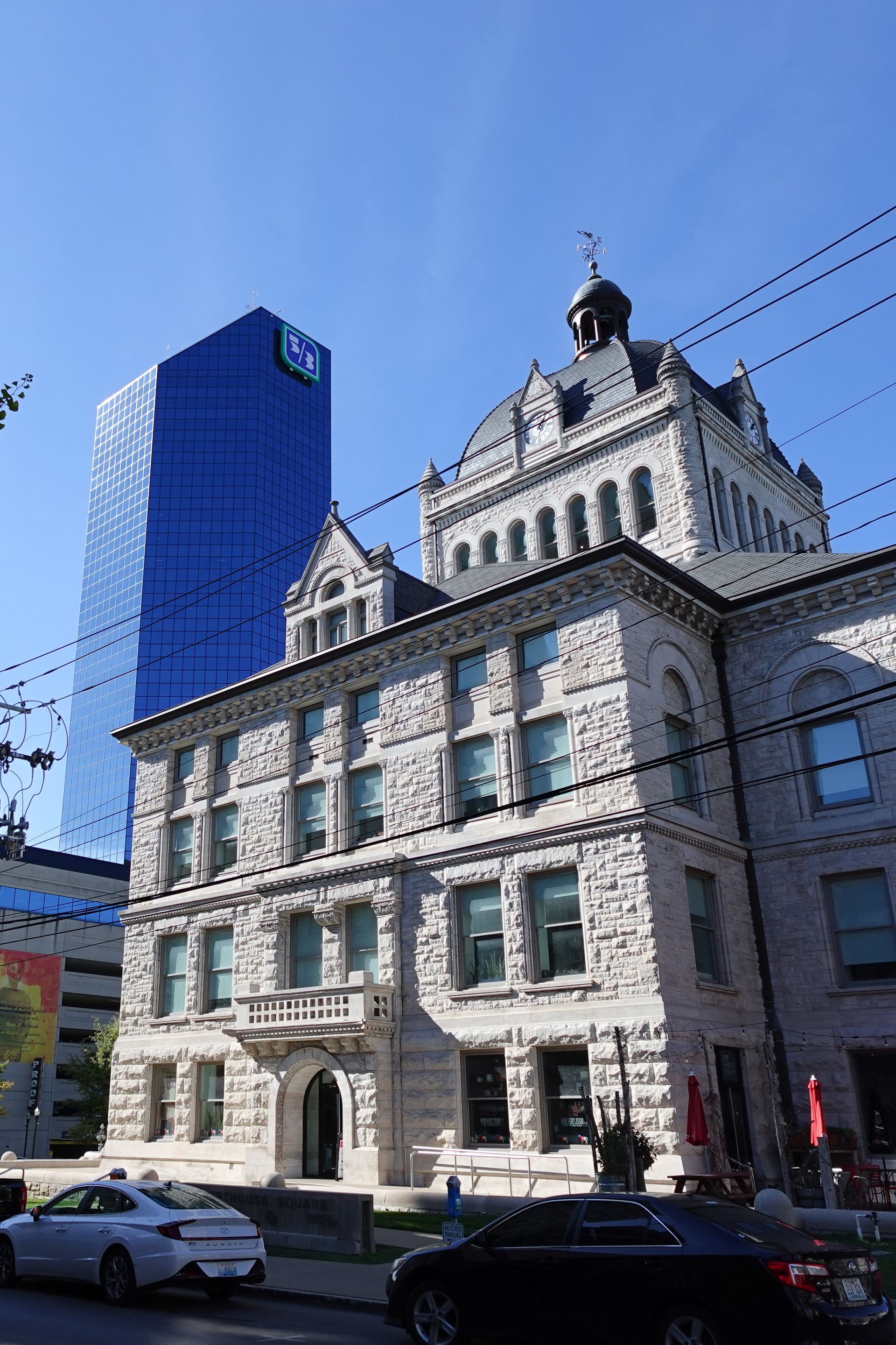 Tall blue building behind square limestone building in downtown Lexington, KY.