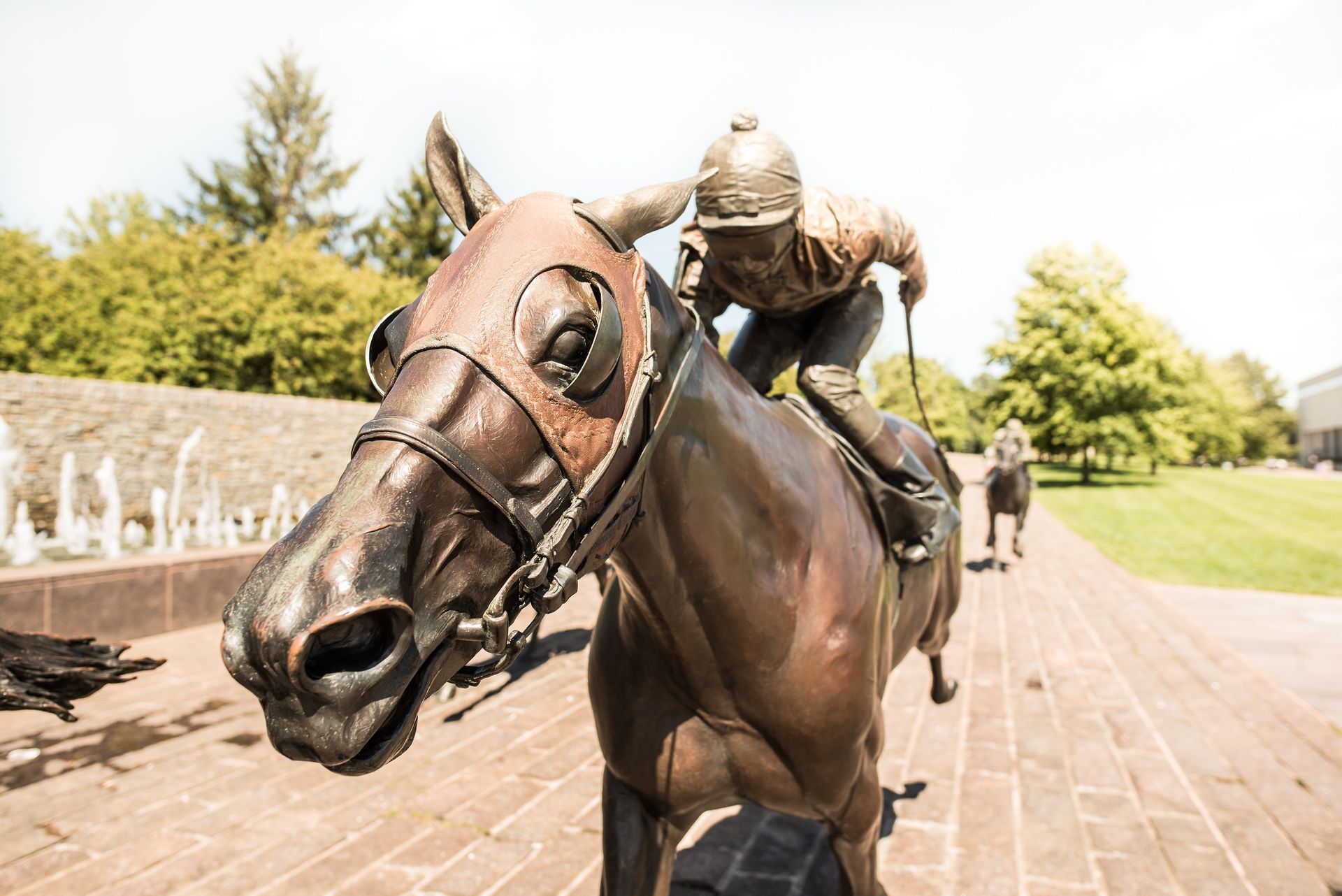 Bronze statue of a horse and jockey; set outside on a brick pathway, sunny day.