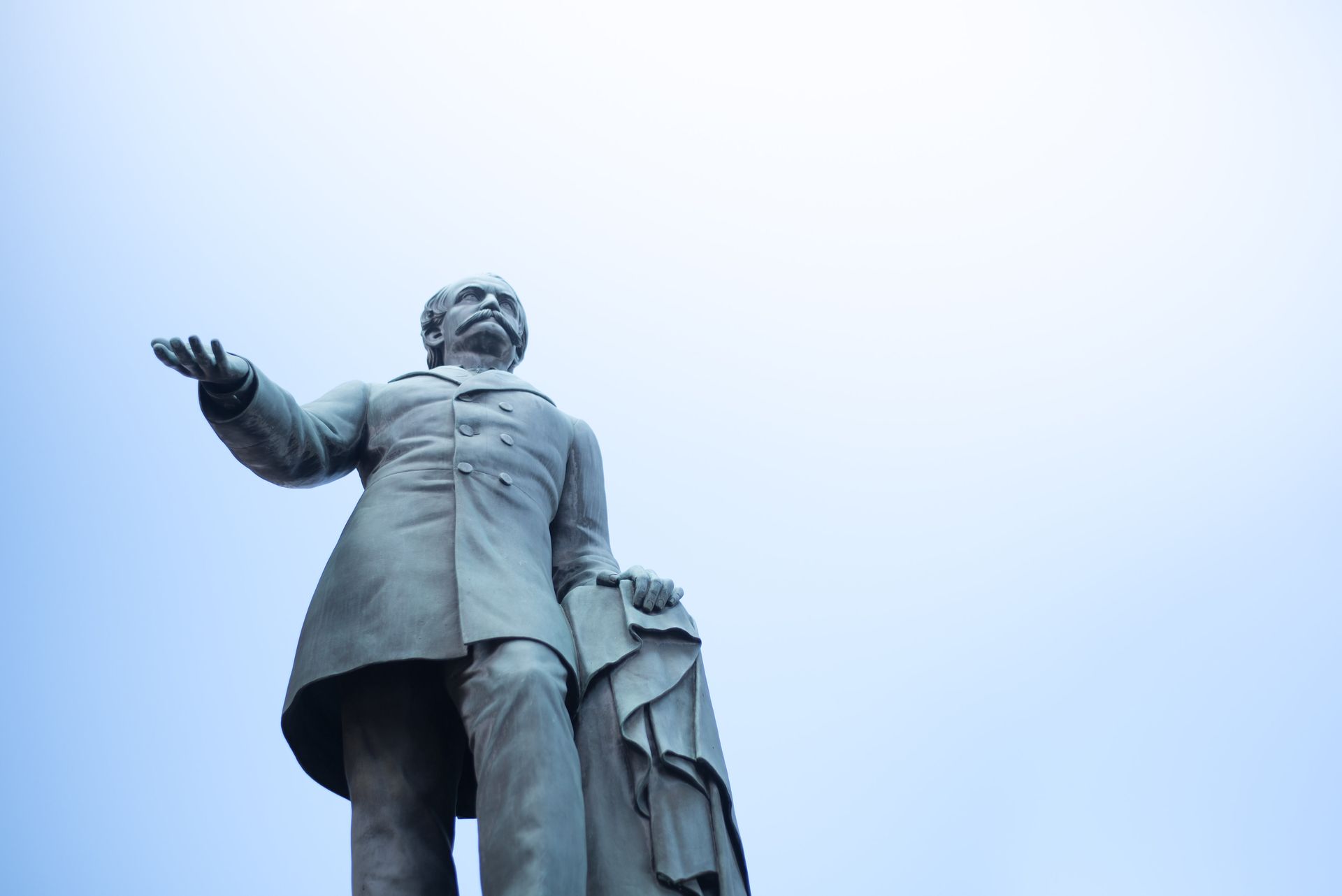 Statue of a man in a coat, arm outstretched, against a blue sky.