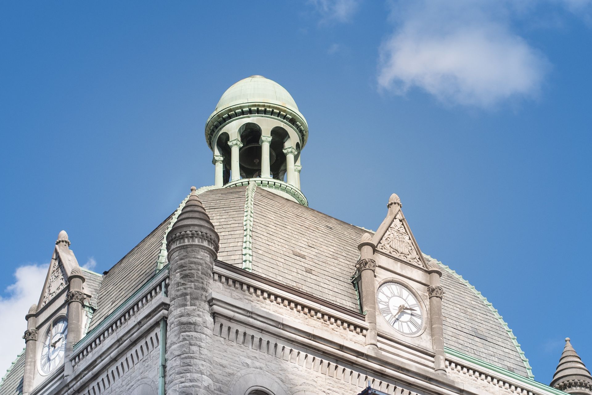 Building with green dome and clock tower against a blue sky.