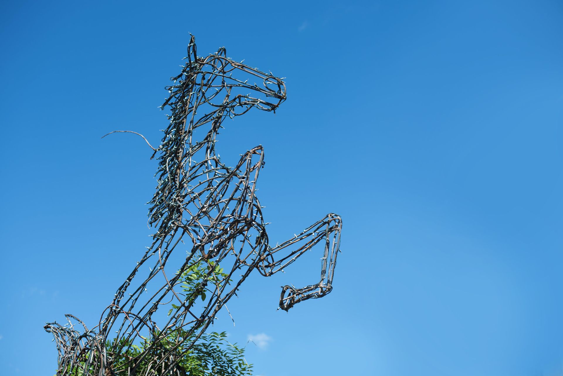 Metal sculpture of a rearing horse against a clear blue sky.