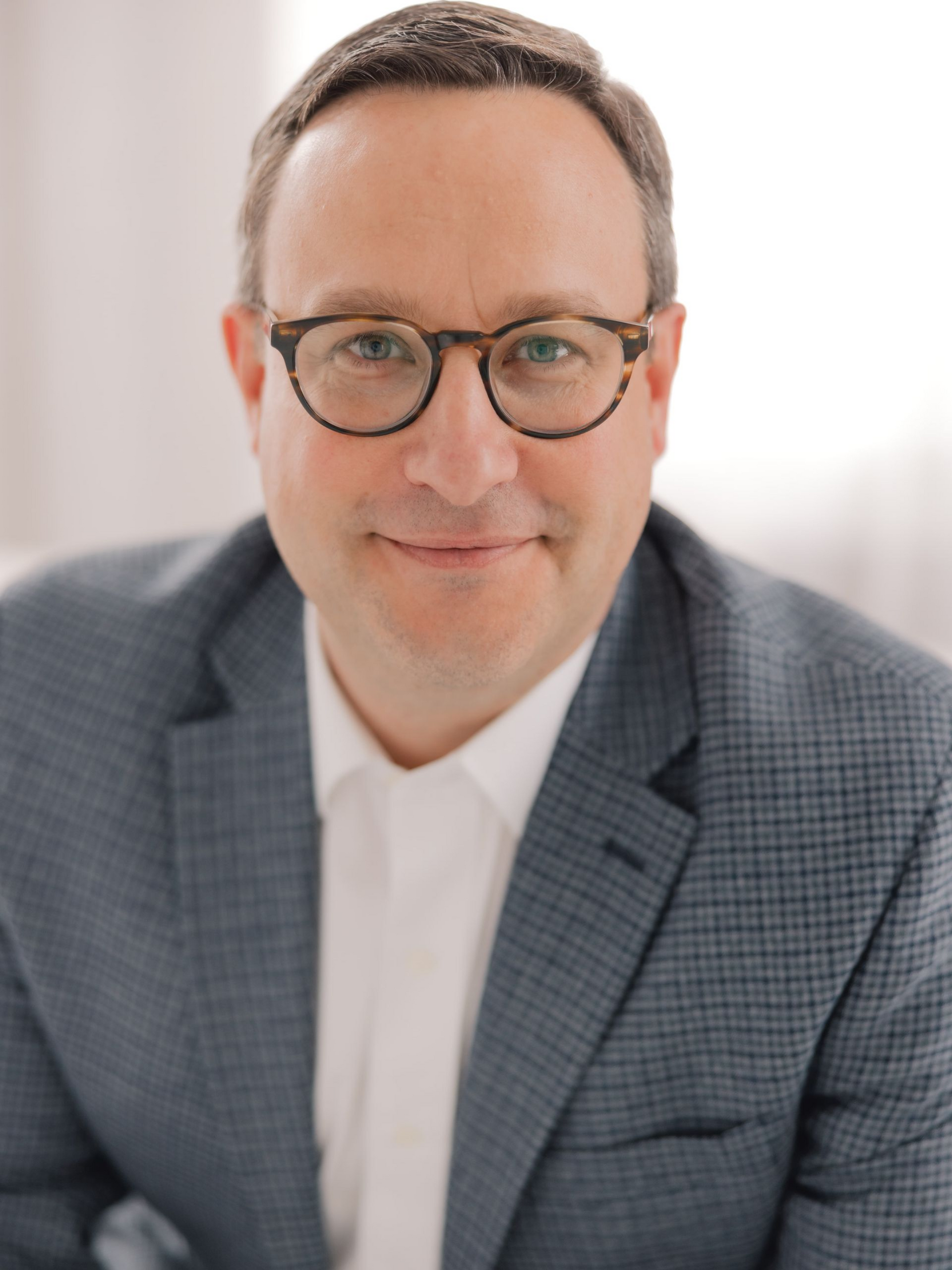 Man in glasses and blazer, smiling.