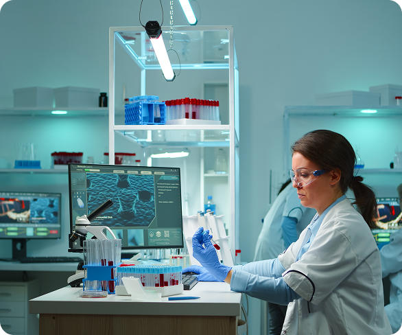 Scientist in lab coat and gloves working with test tubes, looking at a sample, computer screens in background.