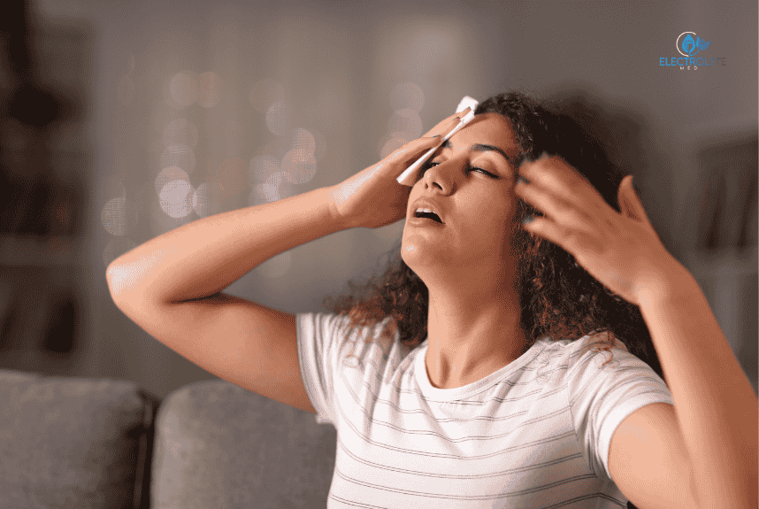 Woman sweating, wiping her forehead with a cloth, indoors. Looks distressed, possibly from heat.